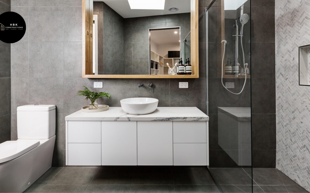Modern bathroom renovation featuring grey tiles, white floating vanity, vessel sink, glass shower with herringbone feature wall, and wall-mounted tapware.